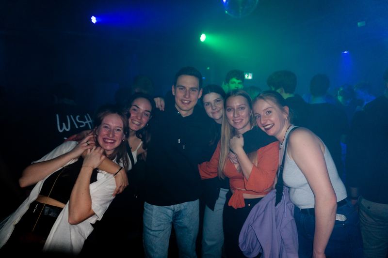 Group of friends posing close together on a dance floor under blue and green club lights.